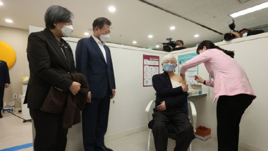 문재인 대통령이 26일 서울 마포구보건소를 방문, 재활시설 종사자인 김윤태 의사(푸르메 넥슨어린이 재활병원)가 아스트라제네카(AZ) 백신을 접종받는 모습을 지켜보고 있다. 연합뉴스